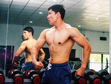 Asyalı genç adam kaslarını bir camın önünde geriyor.