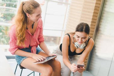Two beautiful young women playing phone and tablet. concept of r