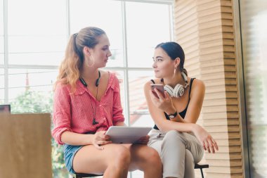 Two beautiful young women playing phone and tablet. concept of r