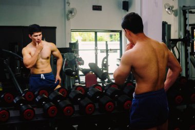 Asyalı genç adam kaslarını bir camın önünde geriyor.