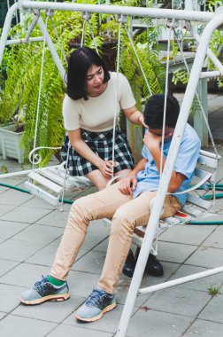 Kız kardeşi üzgün erkek kardeşini bir salıncakta otururken teselli ediyor.