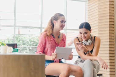 Two beautiful young women playing phone and tablet. concept of r