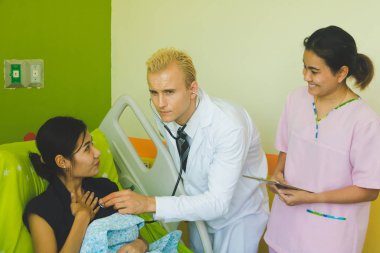 Doktor ve hemşire sethoscop kullanarak kalbi dinliyorlar.