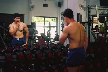 Asyalı genç adam kaslarını bir camın önünde geriyor.