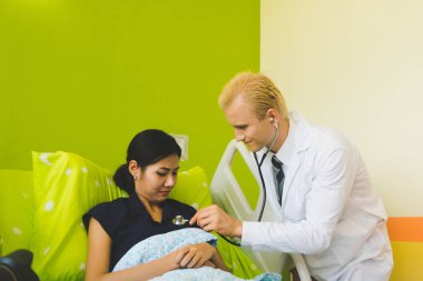 Doktor ve hemşire sethoscop kullanarak kalbi dinliyorlar.