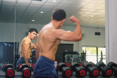 Asyalı genç adam kaslarını bir camın önünde geriyor.