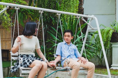 Kız ve erkek kardeş evin bahçesinde salıncak oynuyorlar.