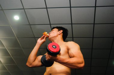 Asyalı adamın kasları var pizza yiyor ve dambılları kaldırıyor.