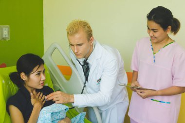 Doktor ve hemşire sethoscop kullanarak kalbi dinliyorlar.