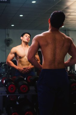 Asyalı genç adam kaslarını bir camın önünde geriyor.