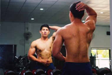 Asyalı genç adam kaslarını bir camın önünde geriyor.