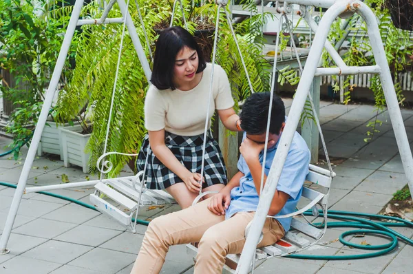 Kız kardeşi üzgün erkek kardeşini bir salıncakta otururken teselli ediyor.