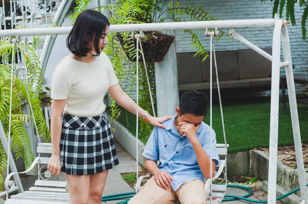 Kız kardeşi üzgün erkek kardeşini bir salıncakta otururken teselli ediyor.