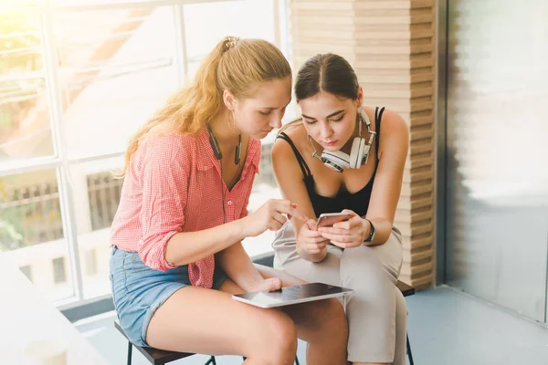 Two beautiful young women playing phone and tablet. concept of r