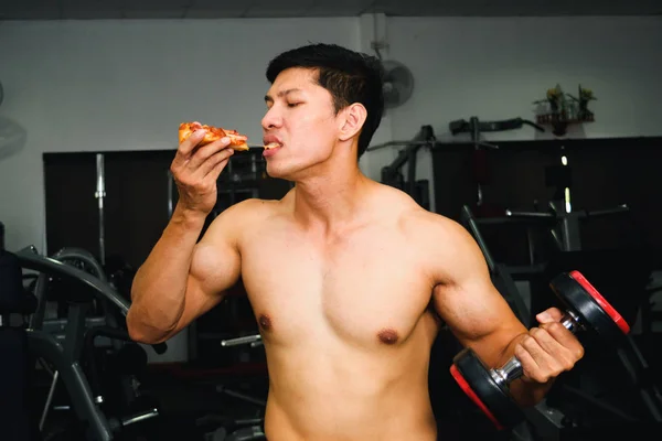 Asiatischer Mann hat Muskeln beim Pizza essen und Hantelheben — Stockfoto