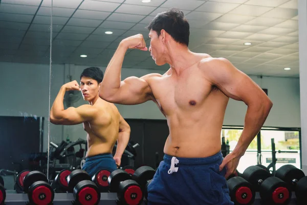 Asiatico giovane uomo flexing suo muscoli in anteriore di un bicchiere in il g — Foto Stock