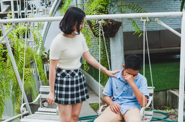 Kız kardeşi üzgün erkek kardeşini bir salıncakta otururken teselli ediyor.