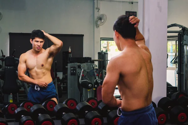 Asyalı genç adam kaslarını bir camın önünde geriyor.