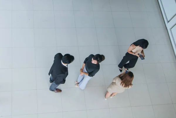 Asian office workers stand and talk in the office lobby.