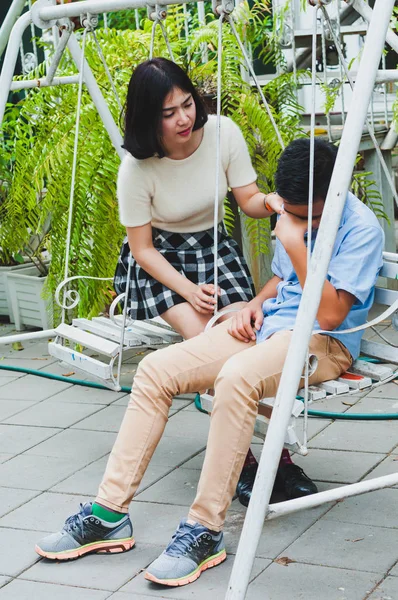 Kız kardeşi üzgün erkek kardeşini bir salıncakta otururken teselli ediyor.