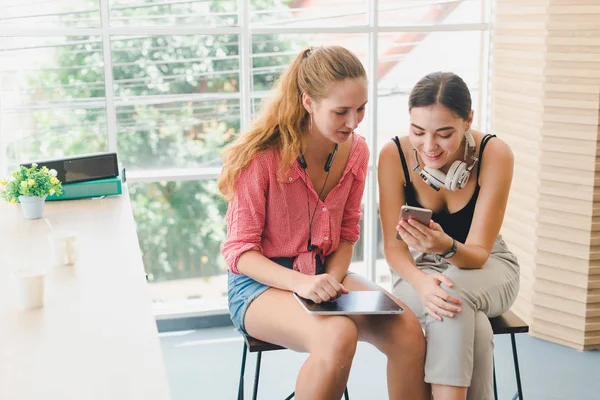 Two beautiful young women playing phone and tablet. concept of r
