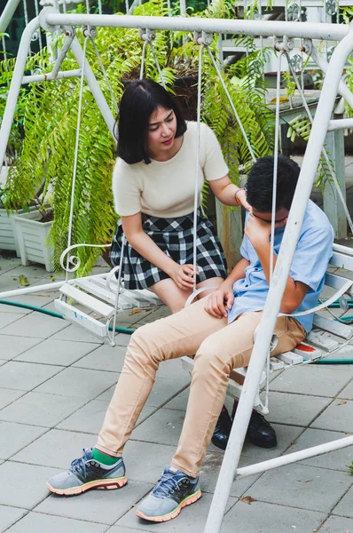 Kız kardeşi üzgün erkek kardeşini bir salıncakta otururken teselli ediyor.