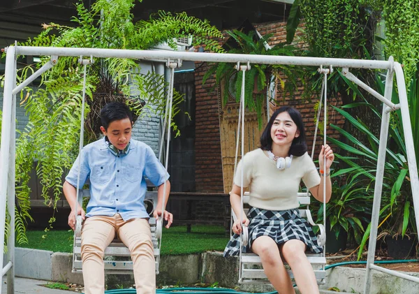 Kız ve erkek kardeş evin bahçesinde salıncak oynuyorlar.