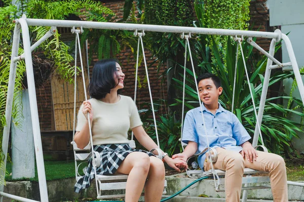 Kız ve erkek kardeş evin bahçesinde salıncak oynuyorlar.