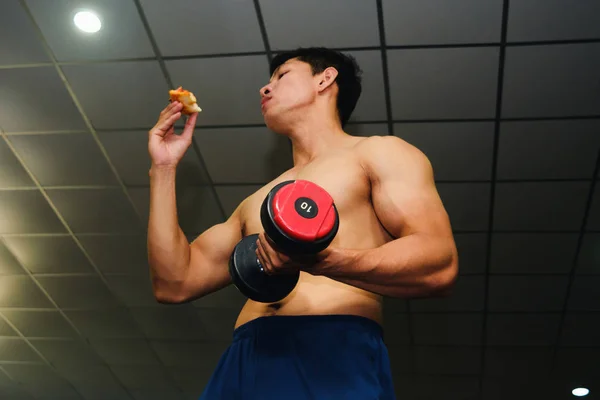 アジアの男は筋肉を持っています食べるピザと持ち上げるダンベル — ストック写真