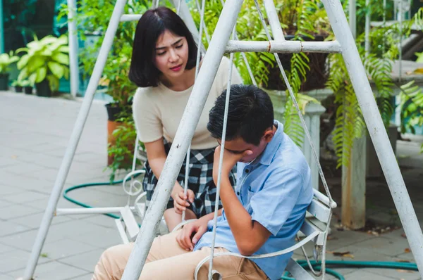 Kız kardeşi üzgün erkek kardeşini bir salıncakta otururken teselli ediyor.