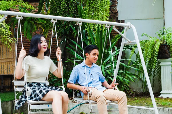 Kız ve erkek kardeş evin bahçesinde salıncak oynuyorlar.