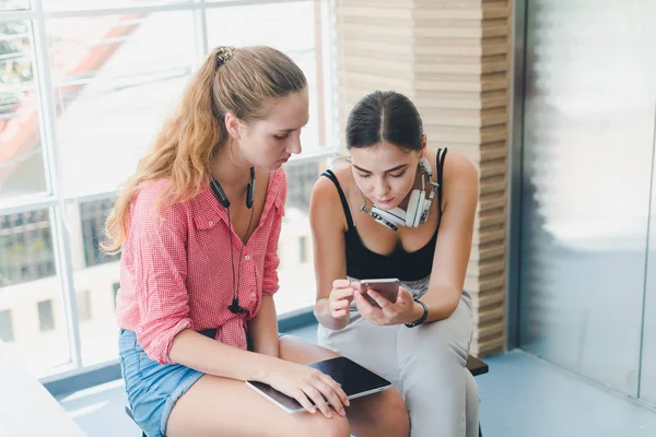 Two beautiful young women playing phone and tablet. concept of r — ストック写真