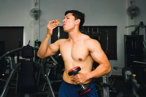 Ázsiai férfi izom eszik pizza és emelő súlyzó — Stock Fotó