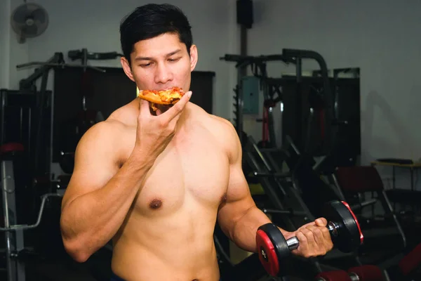 Asiatischer Mann hat Muskeln beim Pizza essen und Hantelheben — Stockfoto