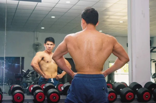 Asiatische junge Mann lässt seine Muskeln vor einem Glas in der g — Stockfoto