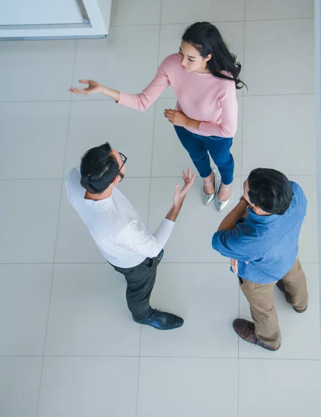 Asian office workers stand and talk in the office lobby.