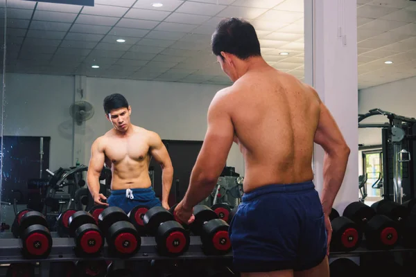 Asiatique jeune homme fléchissant ses muscles devant un verre dans le g — Photo