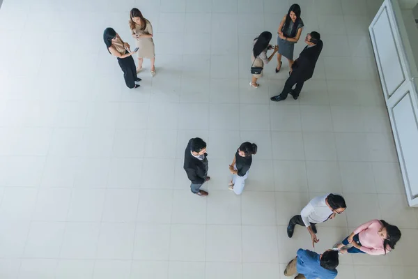 Asian office workers stand and talk in the office lobby.