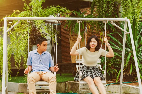 Kız ve erkek kardeş evin bahçesinde salıncak oynuyorlar.