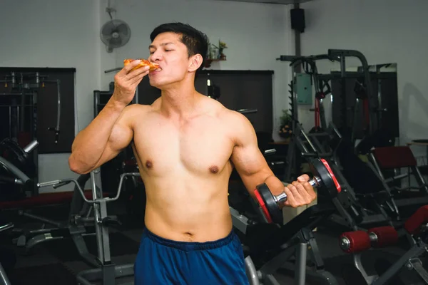 Ásia homem tem muscular comer pizza e levantamento dumbbell — Fotografia de Stock