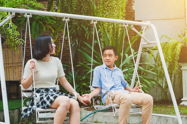 Kız ve erkek kardeş evin bahçesinde salıncak oynuyorlar.