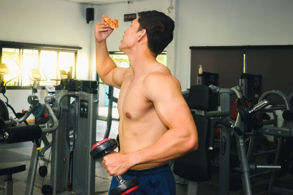 Asyalı adamın kasları var pizza yiyor ve dambılları kaldırıyor.