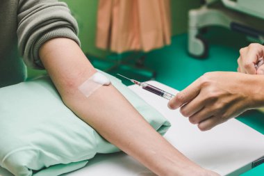 Hemşire şırıngayla hastanın kanını alıyor..