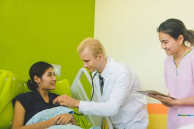 Doktor ve hemşire sethoscop kullanarak kalbi dinliyorlar.