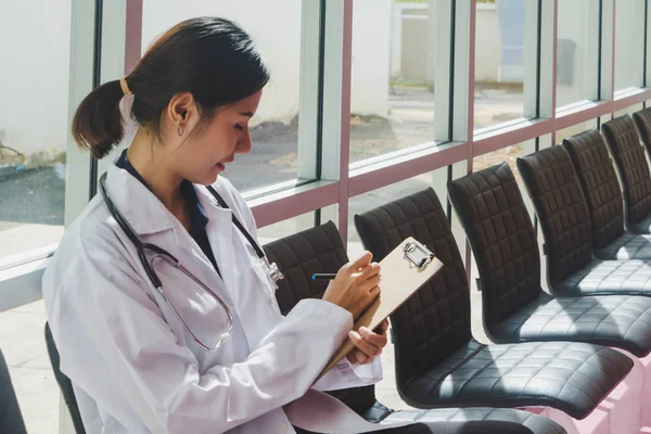 Asiático médico sentado en portapapeles escritura En el pasillo de la —  Fotos de Stock
