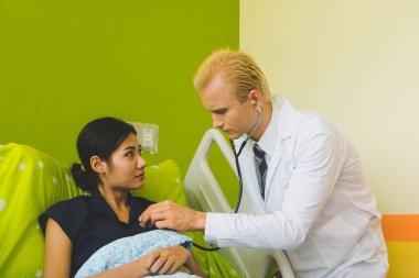 Doktor ve hemşire sethoscop kullanarak kalbi dinliyorlar.