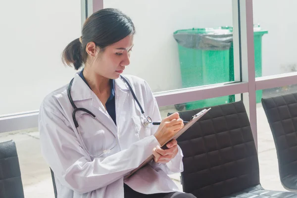 Asiático médico sentado en portapapeles escritura En el pasillo de la —  Fotos de Stock