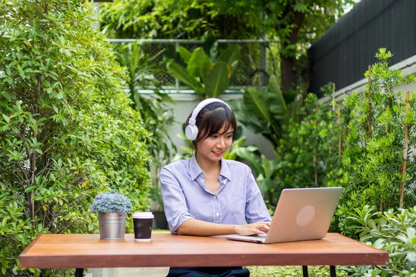 Asian women play notebooks and listen to music in the garden.