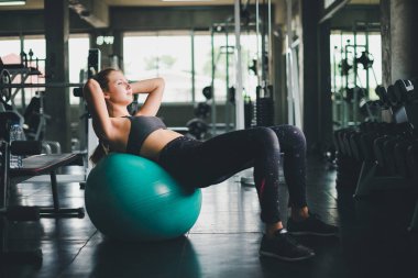 Spor tişörtü giyen güzel bir kadın lastik top, yoga ya da egzersiz topuyla esniyor ve dinleniyor..