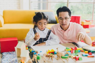 Asyalı baba ve kızı, Noel ve yeni yıl kutlamalarına hazırlanmak için Noel ağaçlarıyla süslenmiş oturma odasındaki masada oyuncak oynuyorlar..